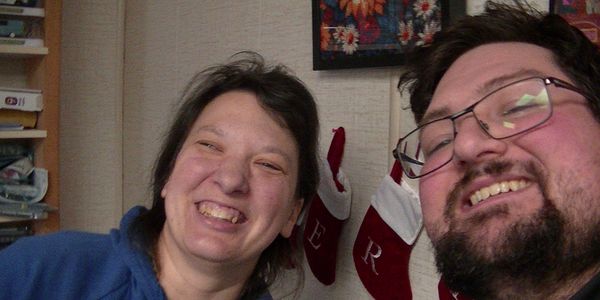 Two people smiling in front of Christmas stockings on a wall.