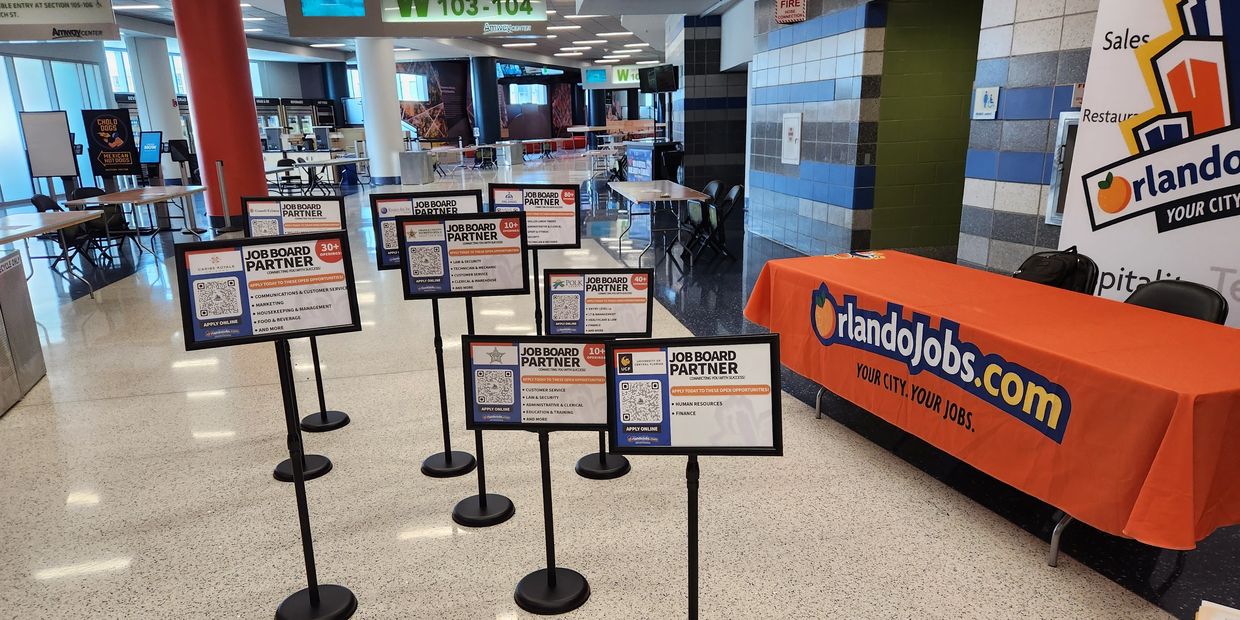 OrlandoJobs.com booth with job board partner signs in a spacious lobby.