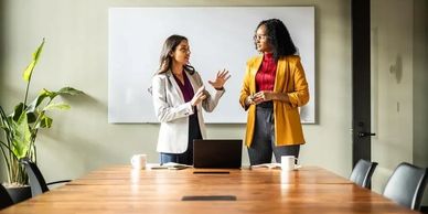 Two professional women discussing in a modern conference room.