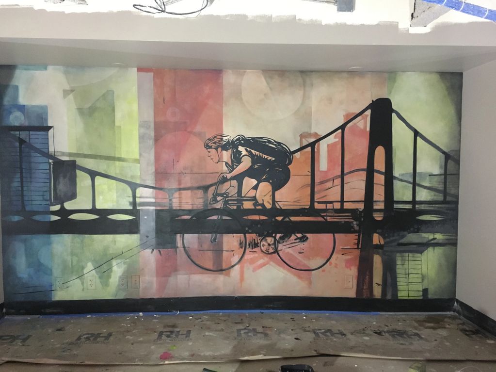 Mural of a cyclist riding across a bridge with colorful cityscape background.