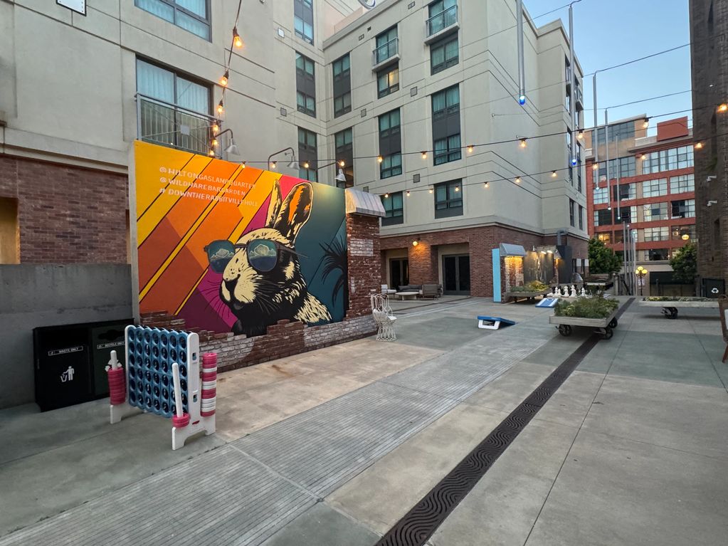 Urban courtyard with a colorful rabbit mural and outdoor games under string lights.