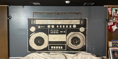 Large black and white boombox mural on gray wall above covered furniture.