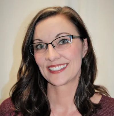 Smiling woman with glasses and wavy brown hair in a maroon top.