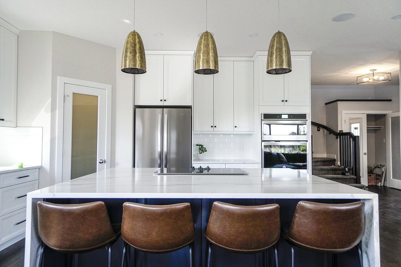 Modern kitchen with marble island and leather bar stools under brass pendant lights.