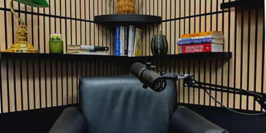 Cozy recording setup with a microphone, black leather chair, and wooden shelves.