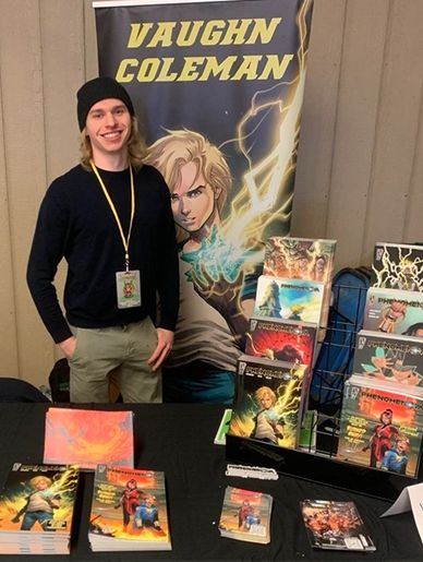 A young man stands beside a display of comic books and merchandise featuring Vaughn Coleman.