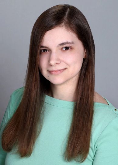 Young woman with long brown hair wearing a mint green top smiling gently.