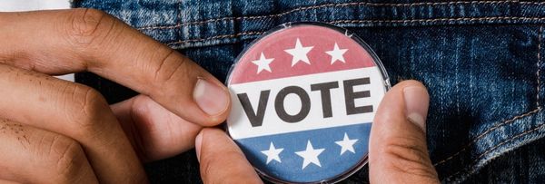 Hands pinning a 'Vote' button on denim fabric.