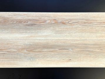 A rectangular wooden plank with light brown grain patterns on a dark surface.