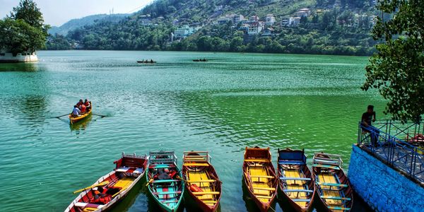 Colorful boats docked by a serene lake with hills and houses in the background.