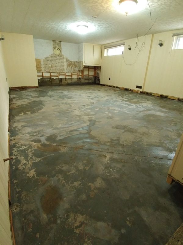 Empty room with worn concrete floor and partially stripped walls under ceiling lights.