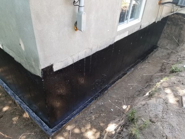 Newly applied waterproofing coating on a house foundation.
