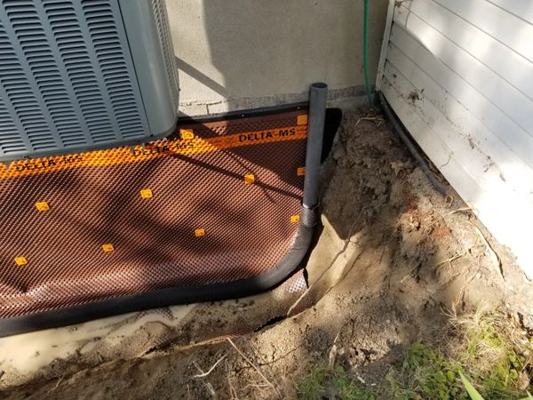 Drainage system installation near house foundation with waterproof membrane and pipe.