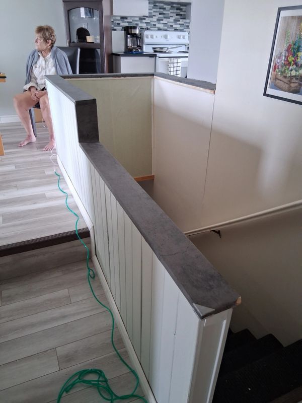 Indoor stairwell with white railing and a woman sitting in the background.