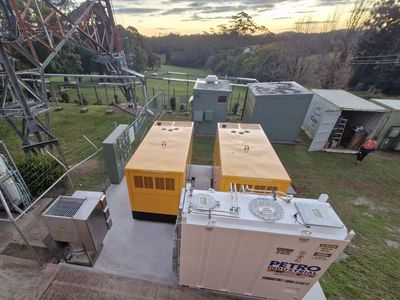 Industrial fuel containers and equipment near a fenced area with a large metal structure.