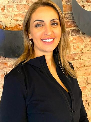 Smiling woman with blonde hair wearing a black zip-up jacket in front of a brick wall.
