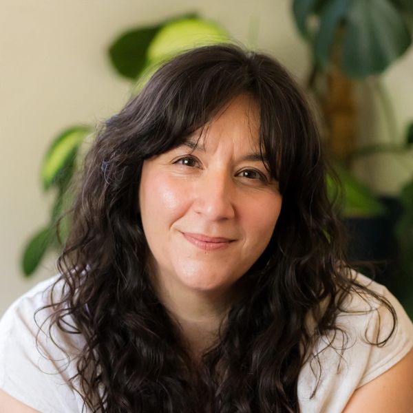 Smiling woman with long dark curly hair in a white shirt.