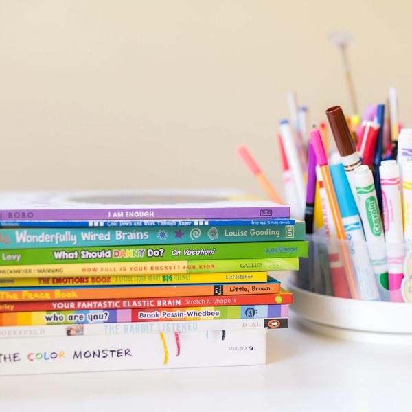 A stack of colorful children's books beside cups of markers.