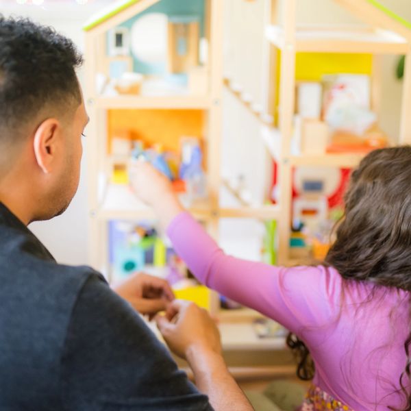 An adult and child playing with a dollhouse.