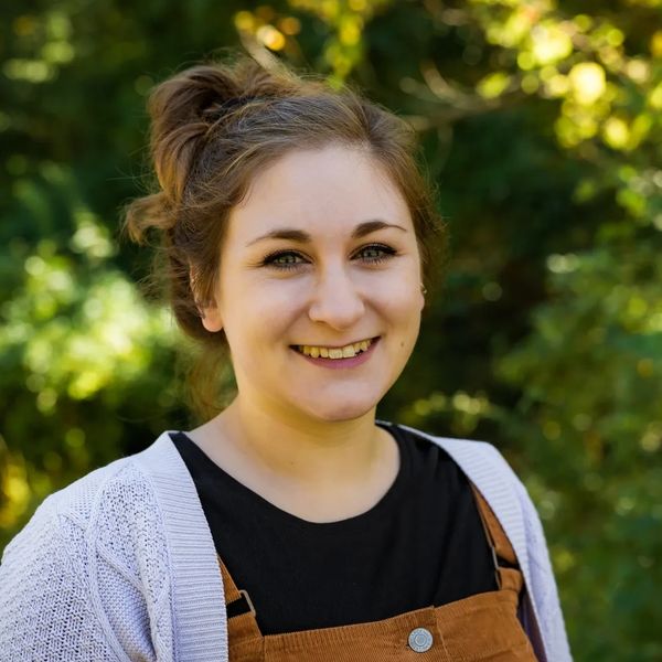 Young woman smiling outdoors with trees in the background.