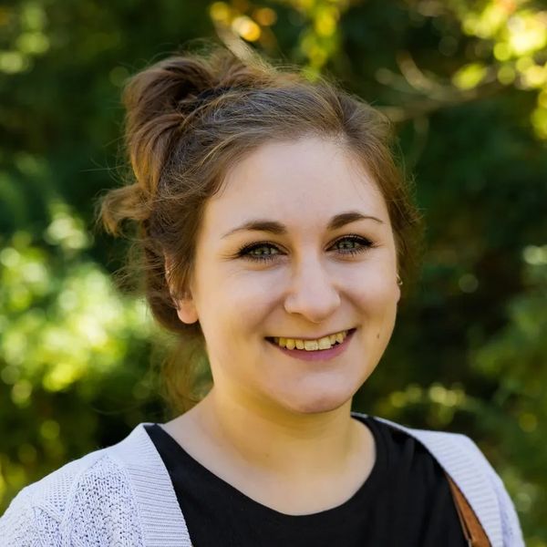 Young woman smiling outdoors with trees in the background.
