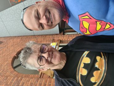 Two men smiling, one in a Batman shirt, the other in a Superman costume.