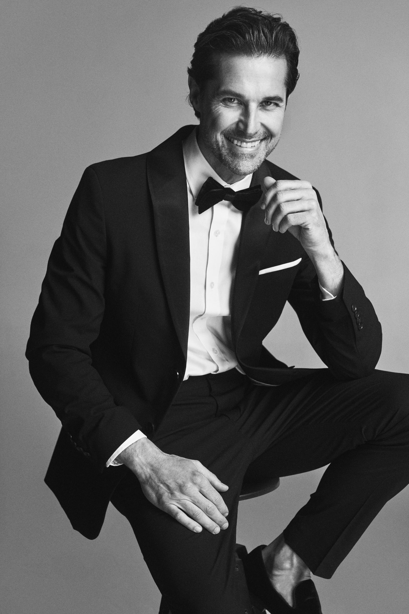 Man in tuxedo smiling and posing confidently.