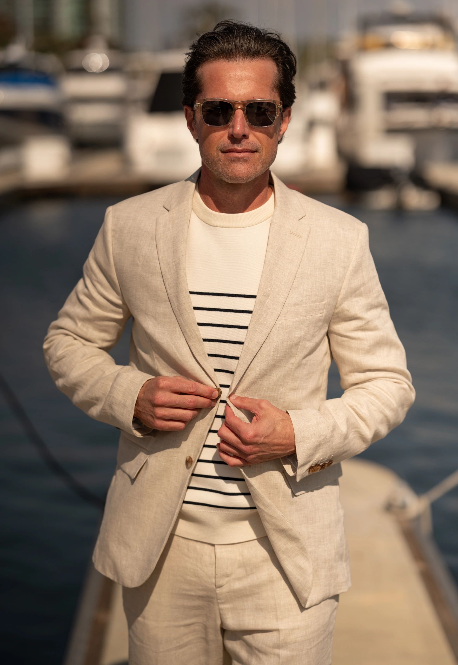 Man in beige suit buttoning jacket near marina.