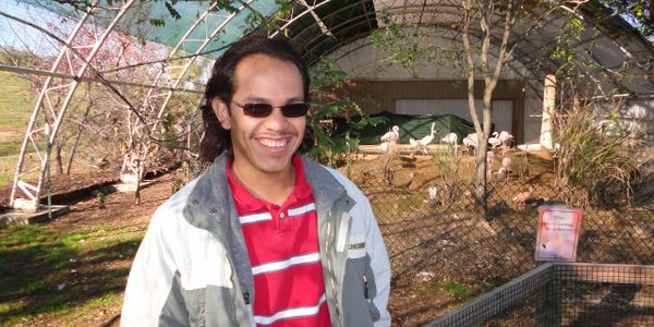 Man wearing red and white striped shirt and sun glasses smiling in front of a flamingo area.