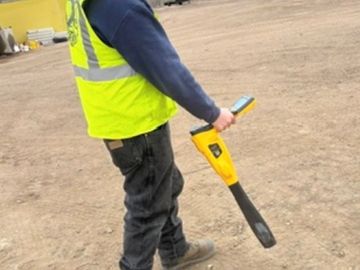 Worker in safety vest using a handheld ground scanning device.