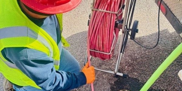 Worker in safety gear handling red cable reel.