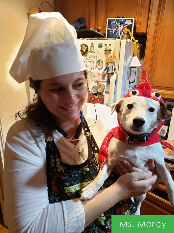 Woman in chef hat holding dog in lobster costume