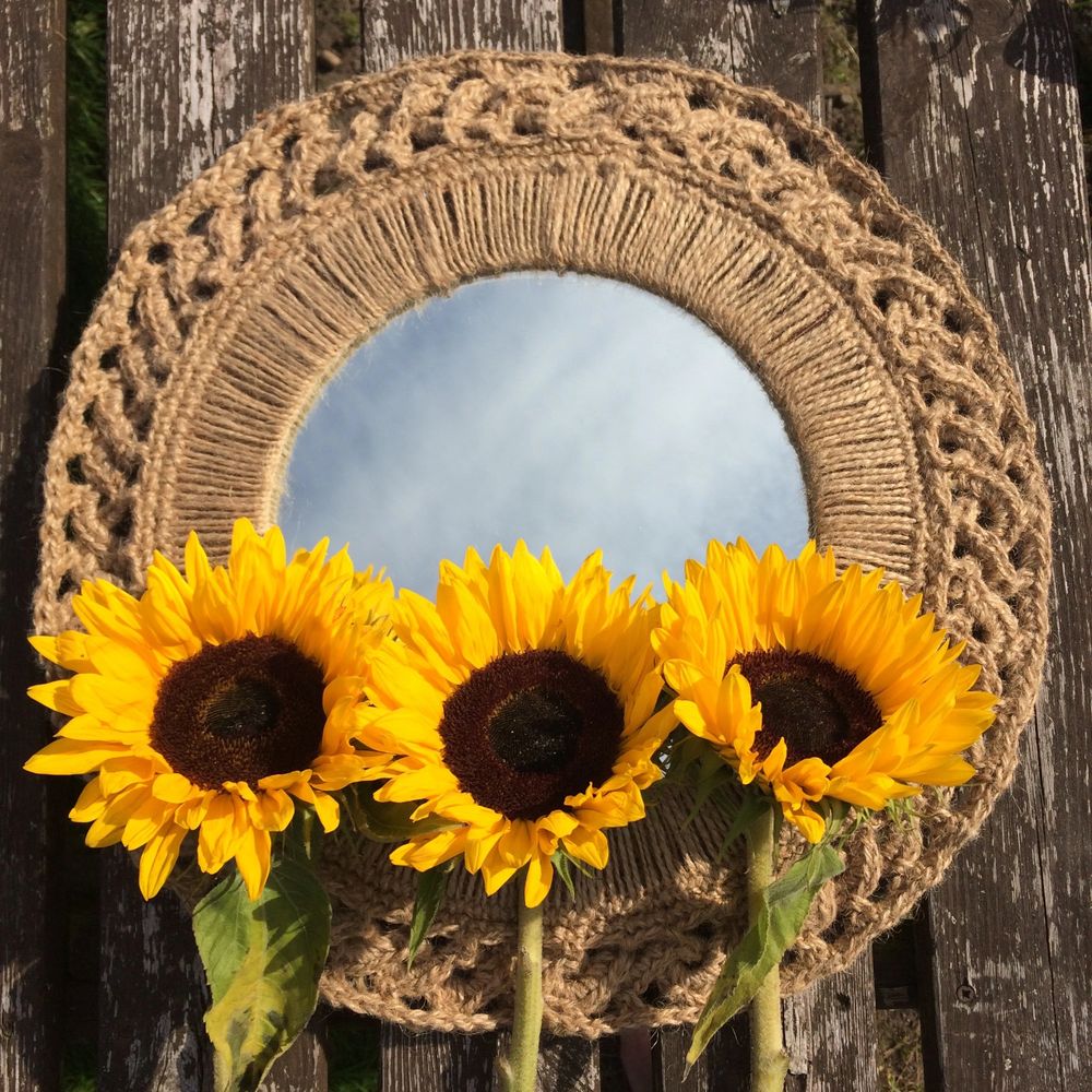 Mirror with crochet jute frame, reflecting a blue sky, with three sunflowers placed on top
