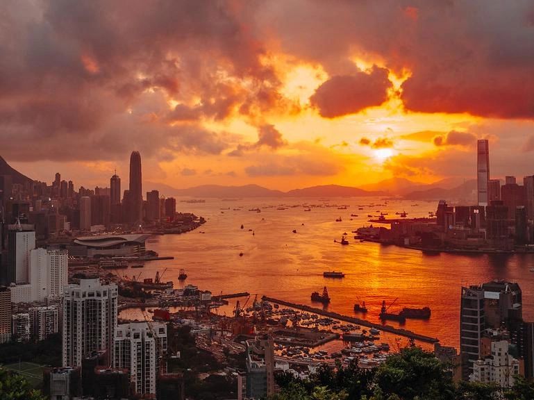 Sunset over a bustling harbor with city skyline.
