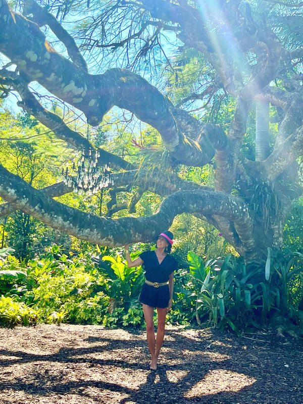 Woman standing under a large, sprawling tree with sunlight filtering through.