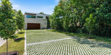 Modern house with green driveway and lush trees.