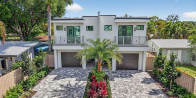 Modern duplex house with gated garages and lush landscaping.