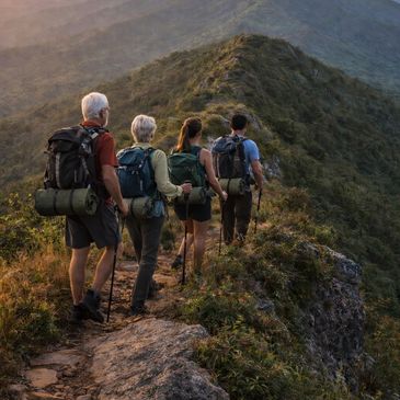 Four hikers trekking along a mountain ridge during sunrise or sunset.