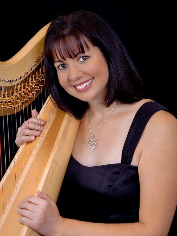 Woman in black dress holding a harp and smiling.