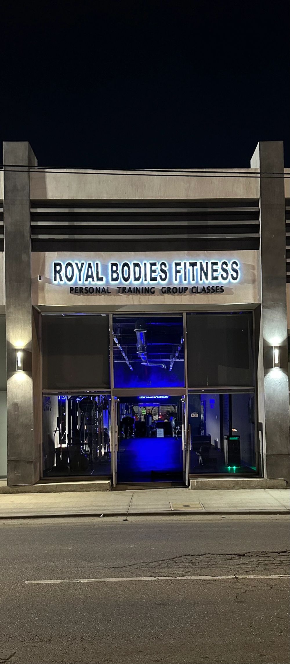 the storefront at night, ROYAL BODIES FITNESS sign, gym equipment visible through the window
