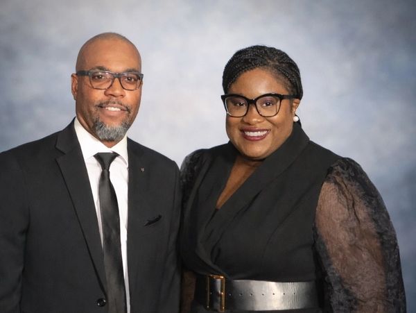 Two people wearing glasses, dressed formally, smiling.