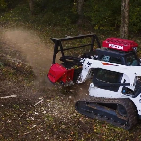 Compact Bobcat machine with Fecon attachment grinding a fallen tree in the forest.