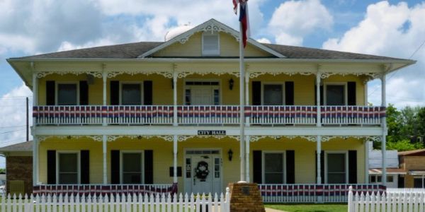 Two-story yellow city hall building with white trim and picket fence.