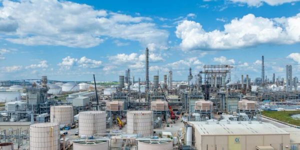 Large industrial oil refinery with storage tanks under blue sky.