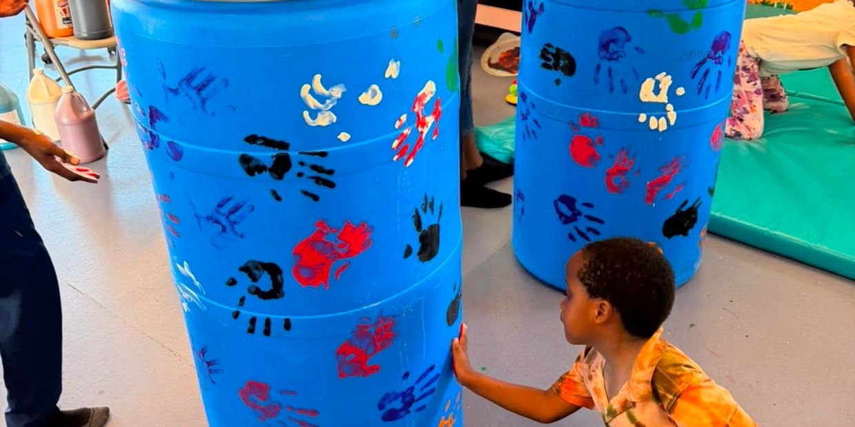 Child touching blue barrels with colorful handprints.