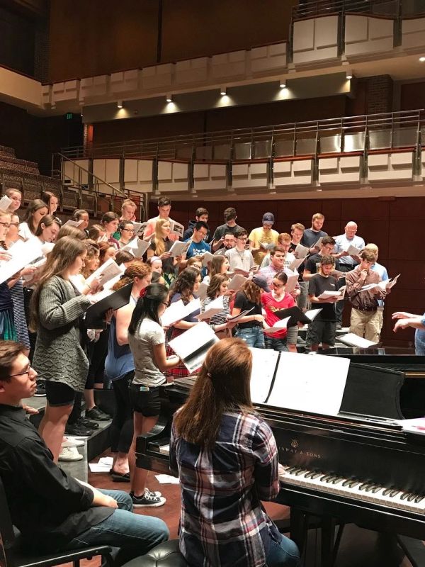 Choir rehearsal with pianist in concert hall.