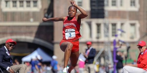 Athlete mid-air during a long jump competition on a track field.