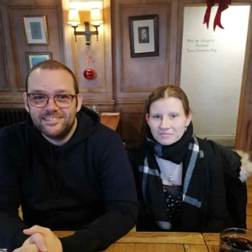 Two people sitting together at a wooden table in a cozy pub or restaurant.