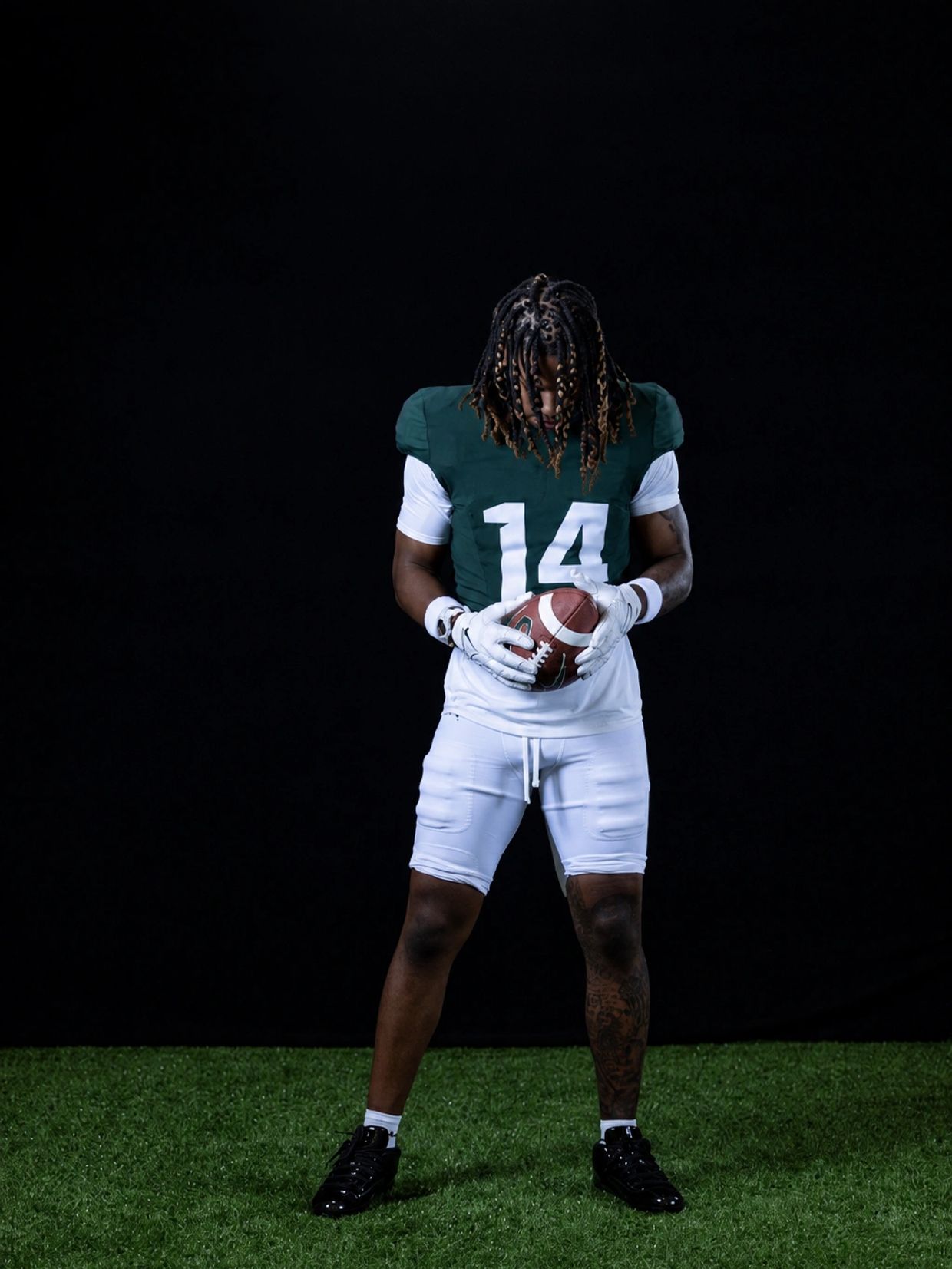Football player holding ball looking down.