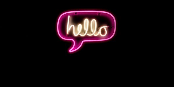 Neon sign glowing with the word "hello" inside a speech bubble.